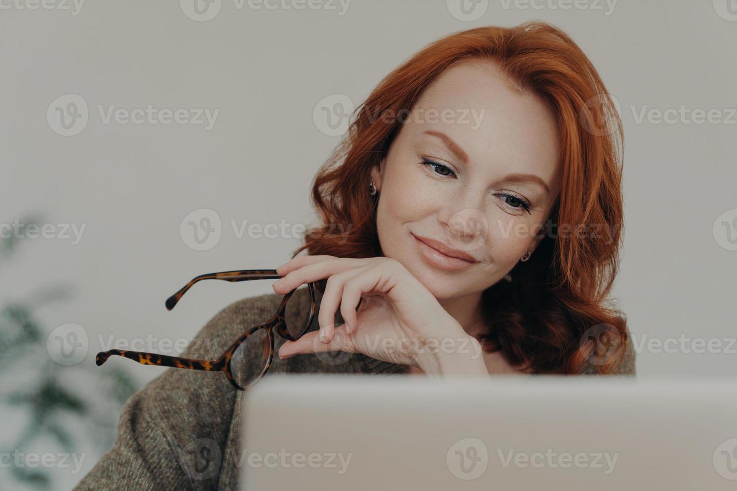 Foto von rothaariger Frau nimmt Brille ab, genießt Freizeit für E-Learning, konzentriert sich auf den Monitor des Laptop-Computers, erledigt Fernjobs. studentin bereitet sich auf prüfungen vor, nutzt moderne technologien