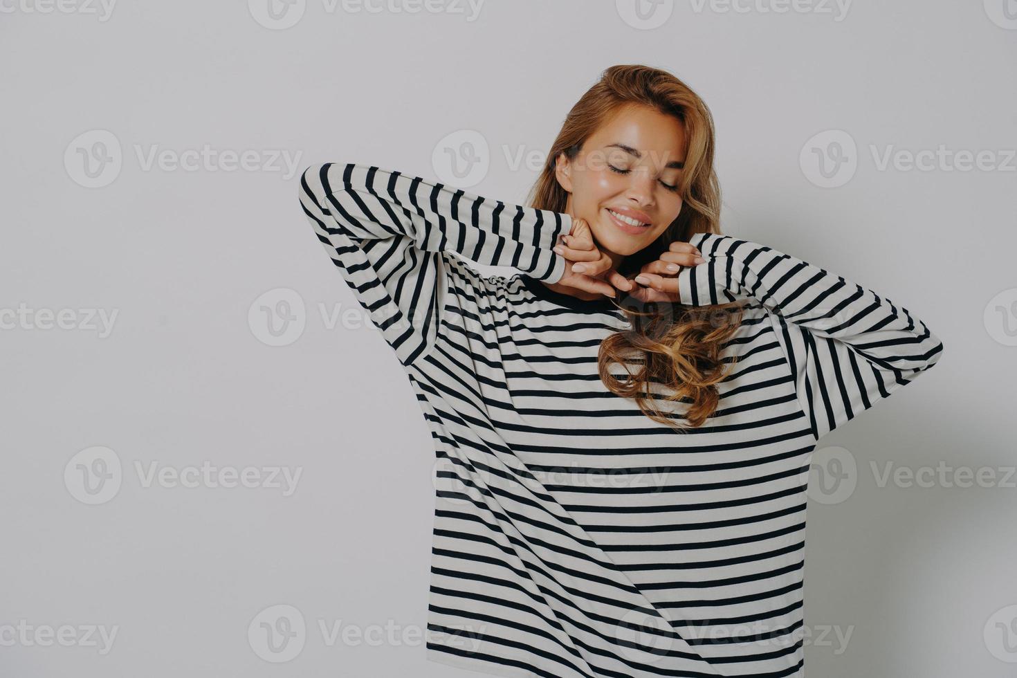 Oberkörperaufnahme einer erfreuten jungen Frau hält die Augen geschlossen, lächelt sanft und zeigt Zähne foto