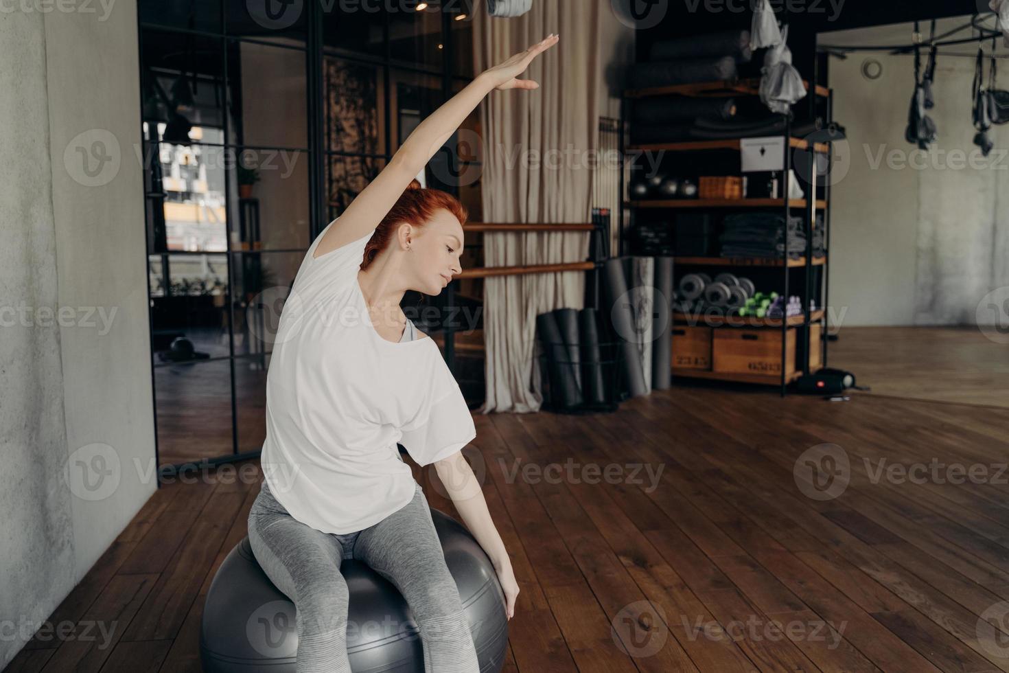junge sportliche Frau, die auf einem großen silbernen Gymnastikball sitzt und sich ausdehnt foto