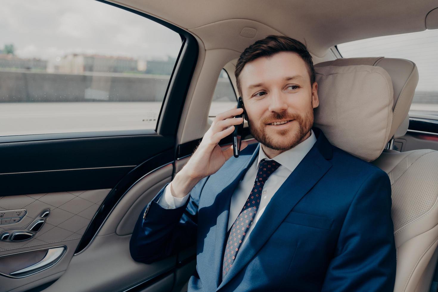 junger gutaussehender geschäftsmann, der fahrt zur konferenz nimmt, während er am telefon spricht foto