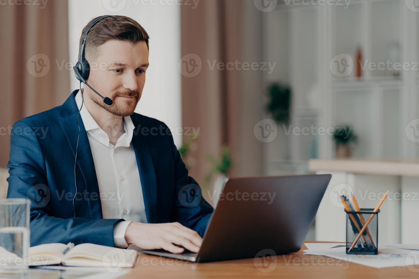 Aufmerksamer Geschäftsmann, der auf den Laptop-Bildschirm schaut, während er von zu Hause aus arbeitet foto