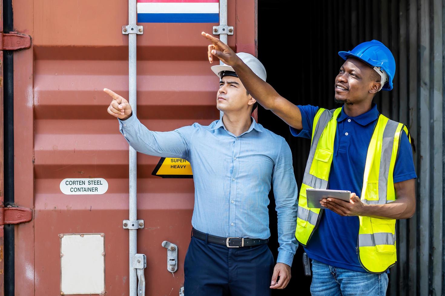 Hafenmanager und ein Kollege, der das Inventar verfolgt, während sie stehen, um die Ladecontainerbox vom Frachtfrachtschiff bei der Frachtcontainerschifffahrt auf einem großen kommerziellen Schifffahrtsdock zu positionieren foto