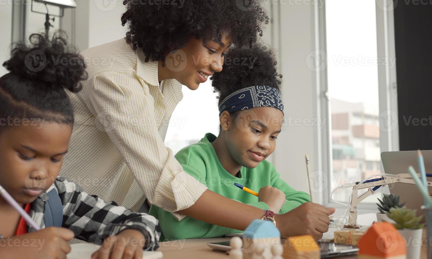 afroamerikanische lehrerin, die mit schülern steht, die schreibunterricht im modernen klassenzimmer unterrichten. foto