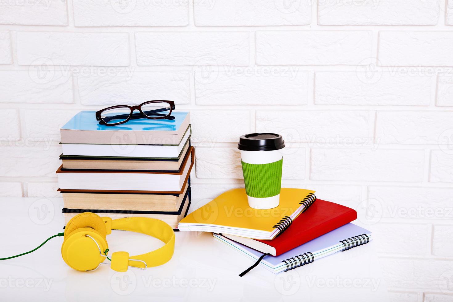 arbeitsplatz- und bildungszubehör auf dem tisch. Tasse Kaffee, Bücher, Gläser, Notizbücher, Kopfhörer. Bildung aufhalten foto
