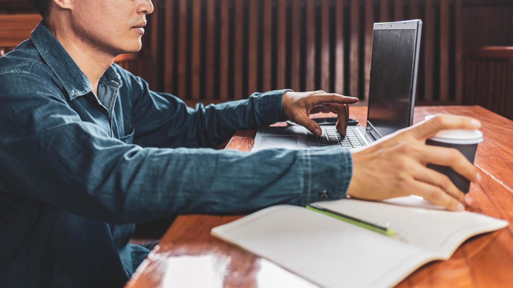 Ein junger Mann mit Brille, der einen Laptop benutzt, der auf einer Tastatur tippt, E-Mails schreibt oder online an einem Computer in seinem Wohnzimmer arbeitet. foto