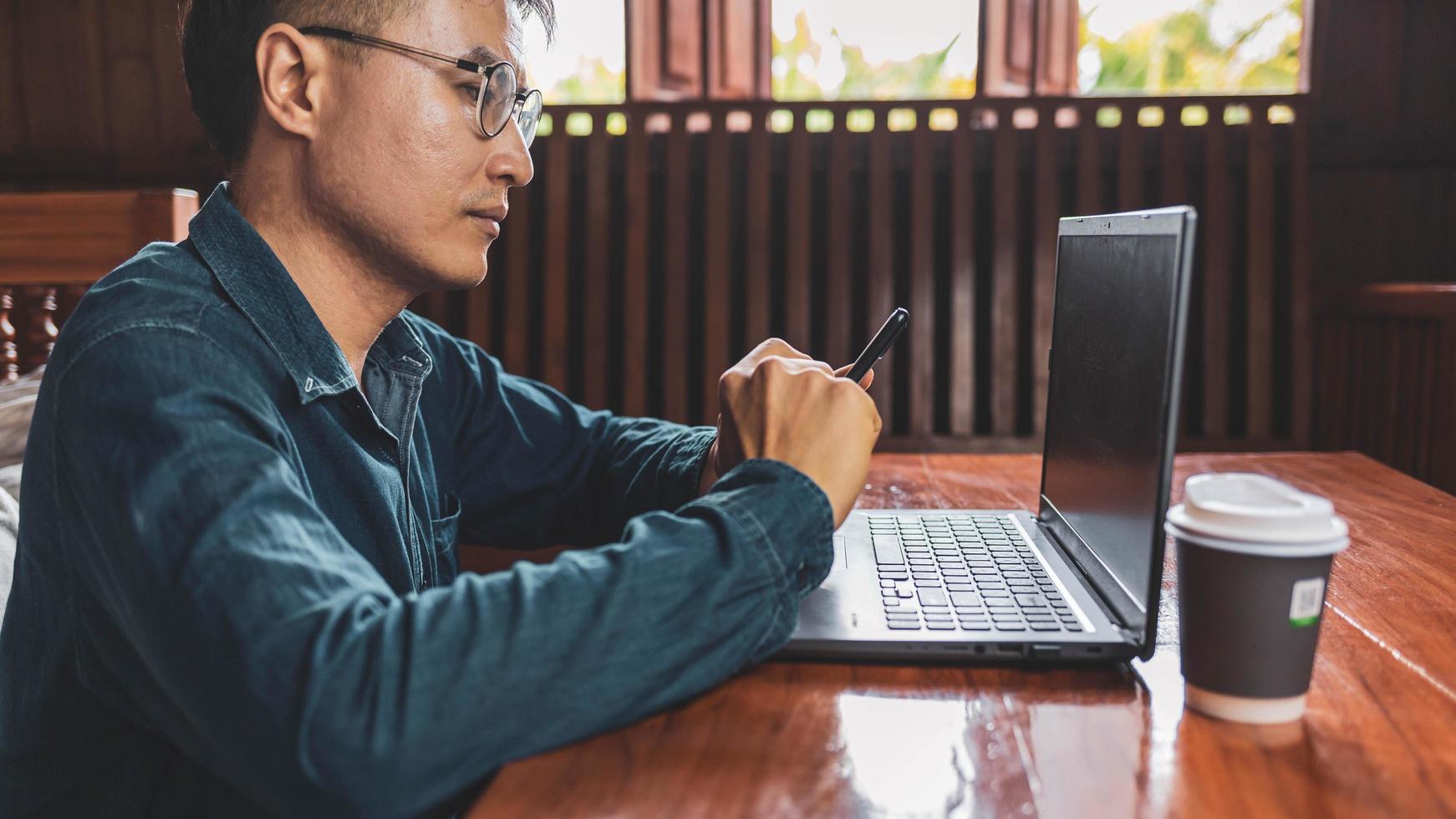 Ein junger Mann mit Brille, der einen Laptop benutzt, der auf einer Tastatur tippt, E-Mails schreibt oder online an einem Computer in seinem Wohnzimmer arbeitet. foto