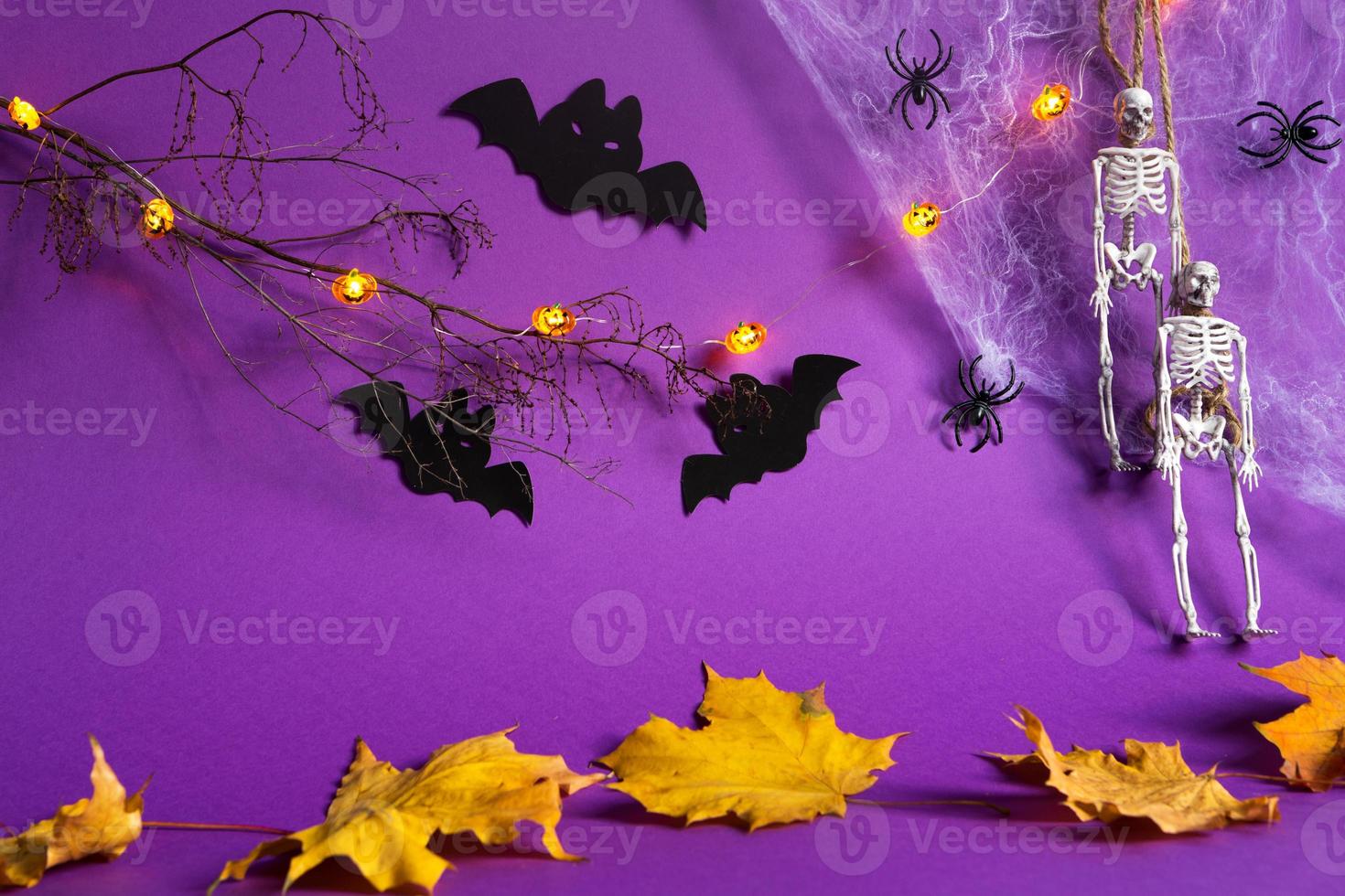 Halloween-Hintergründe von Jack Lantern Kürbis leuchtende Girlande, Spinnennetz, Skelett an einem Seil, Spinnen und schwarze Fledermäuse auf einem violetten Hintergrund mit trockenen gelben Blättern. Horror und ein gruseliger Urlaub foto