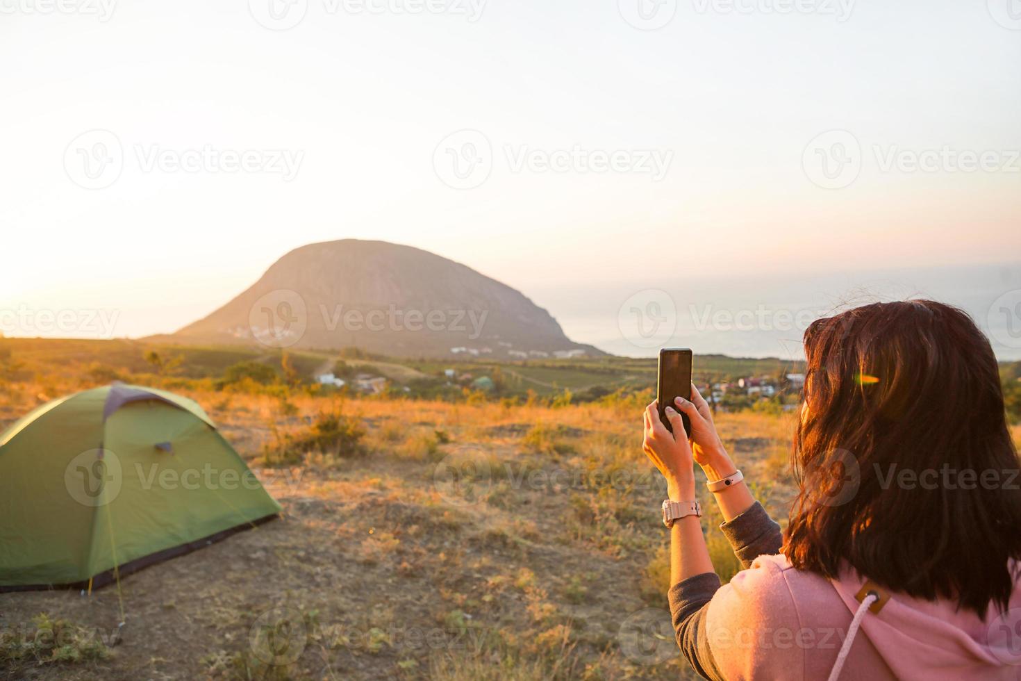 Frau fotografiert den Sonnenaufgang in den Bergen mit ihrem Handy. Selfie bei aufgehender Sonne. Panoramablick auf das Meer und Ayu-Dag. Camping, Outdoor-Aktivitäten, Sportbergwandern, Familienreisen. Krim. foto