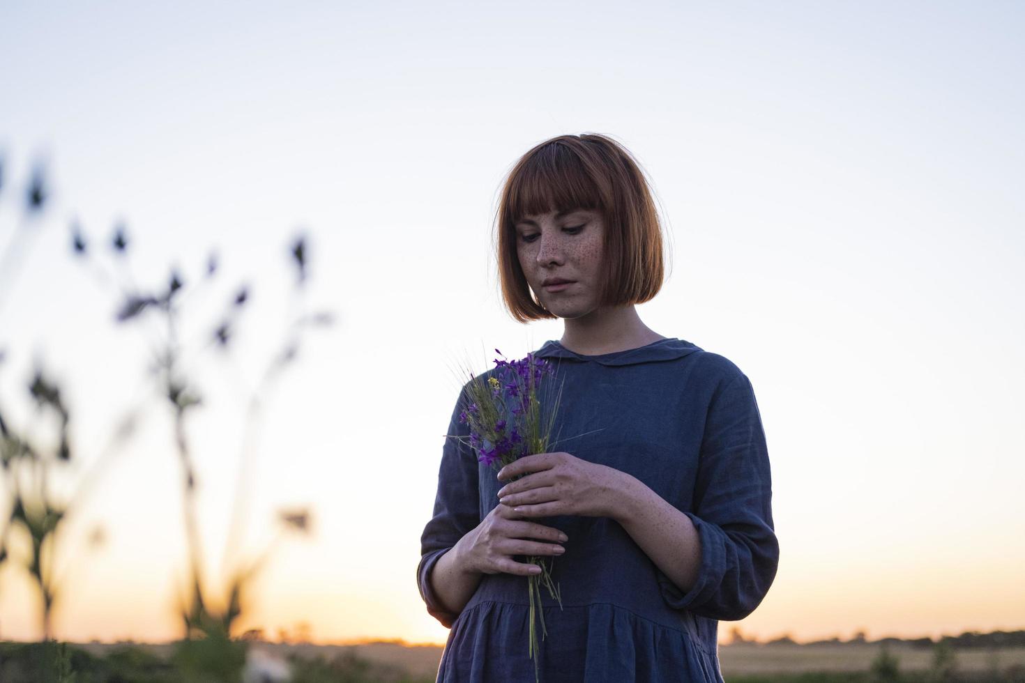 Junge rothaarige Frau mit Sommersprossen in handgefertigtem Vintage-Kleid geht auf Feldern mit Blumen spazieren foto