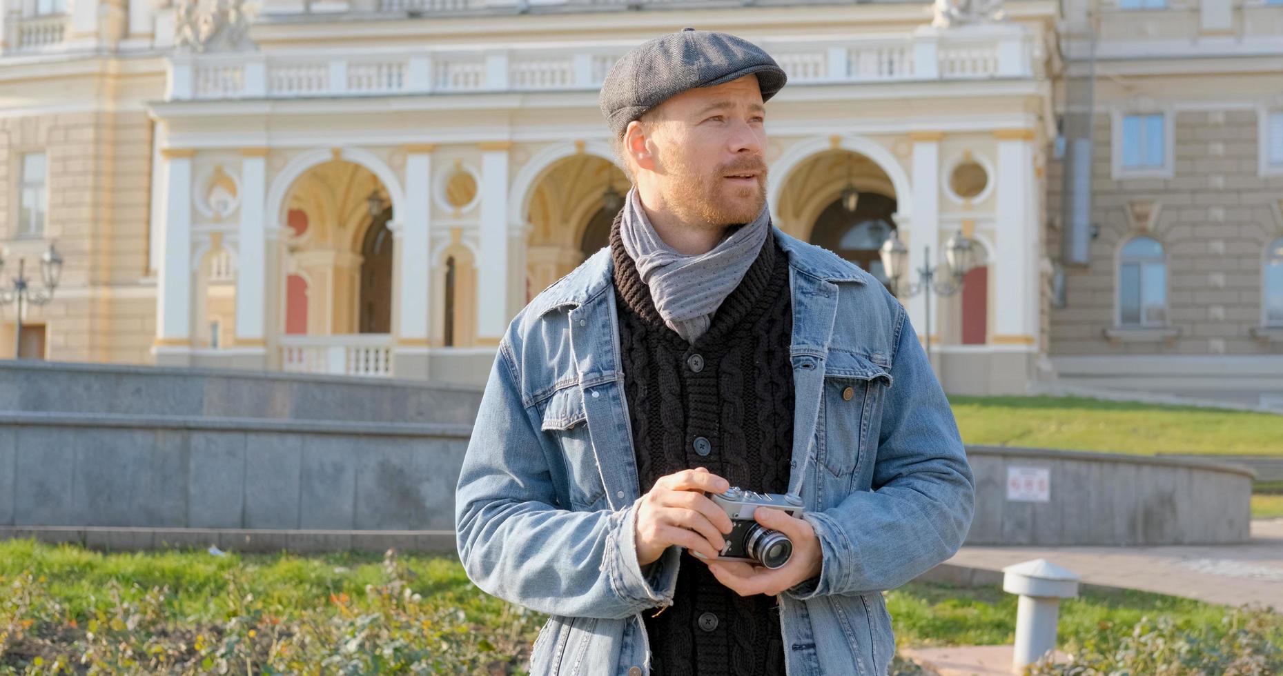 junger gutaussehender männlicher reisender mit filmkamera macht straßenfotos foto