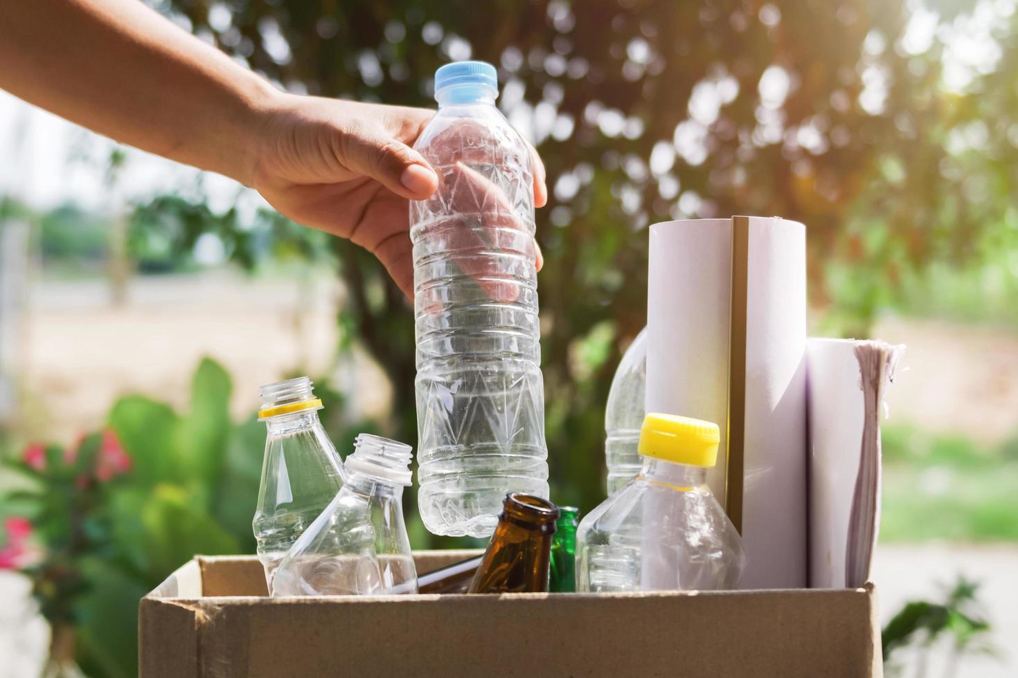 hand, die müllflaschenplastik hält, das zur reinigung in den recyclingbeutel gelegt wird foto