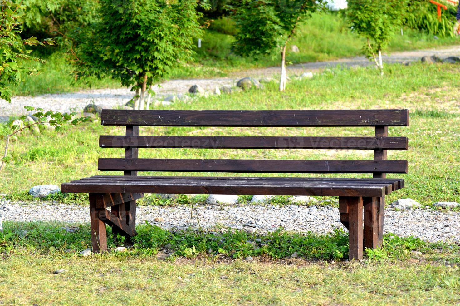 braune Holzbank im Park. Sommer sonniger Tag. grünes Gras und Bäume. Ruhe- und Entspannungsbereich. leere Bank zum Sitzen. Außenmaterial Holz. foto