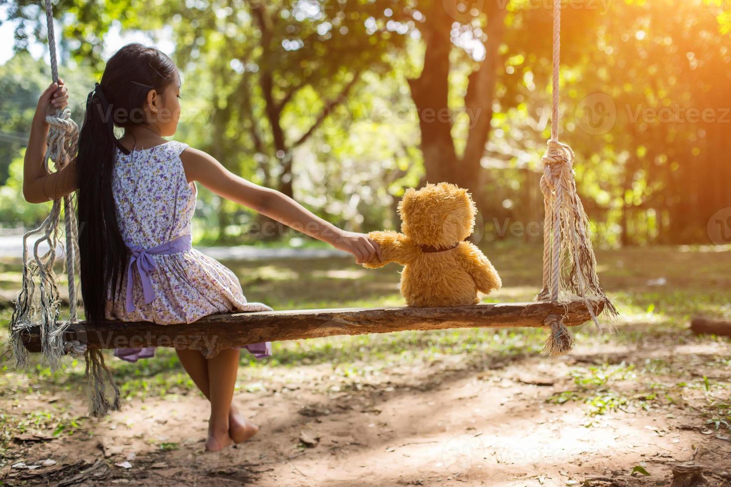 Ein kleines Mädchen und ein Teddybär sitzen auf einer Schaukel. foto