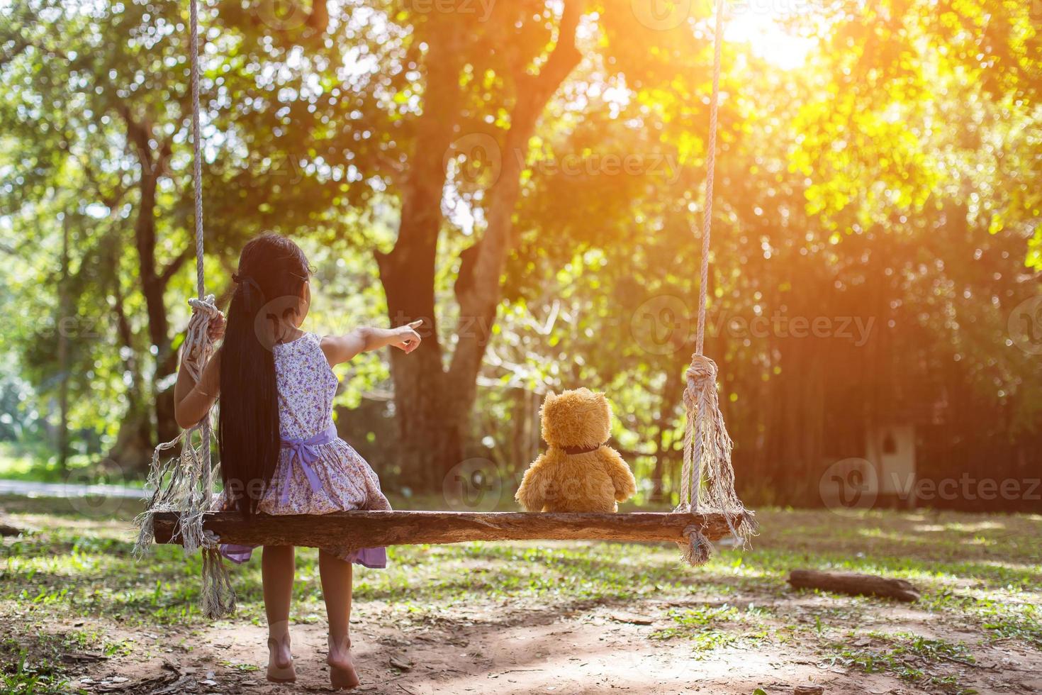 Ein kleines Mädchen und ein Teddybär sitzen auf einer Schaukel. foto