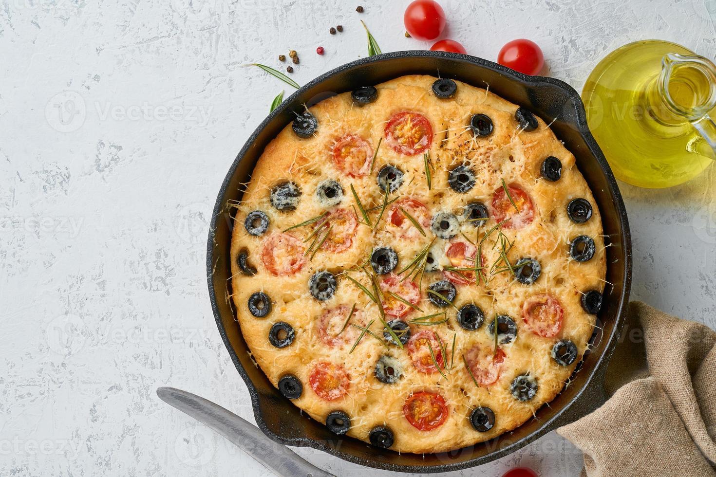 Focaccia, Pizza in der Pfanne, italienisches Fladenbrot mit Tomaten, Oliven und Rosmarin. draufsicht, kopierraum, weißer betonhintergrund foto