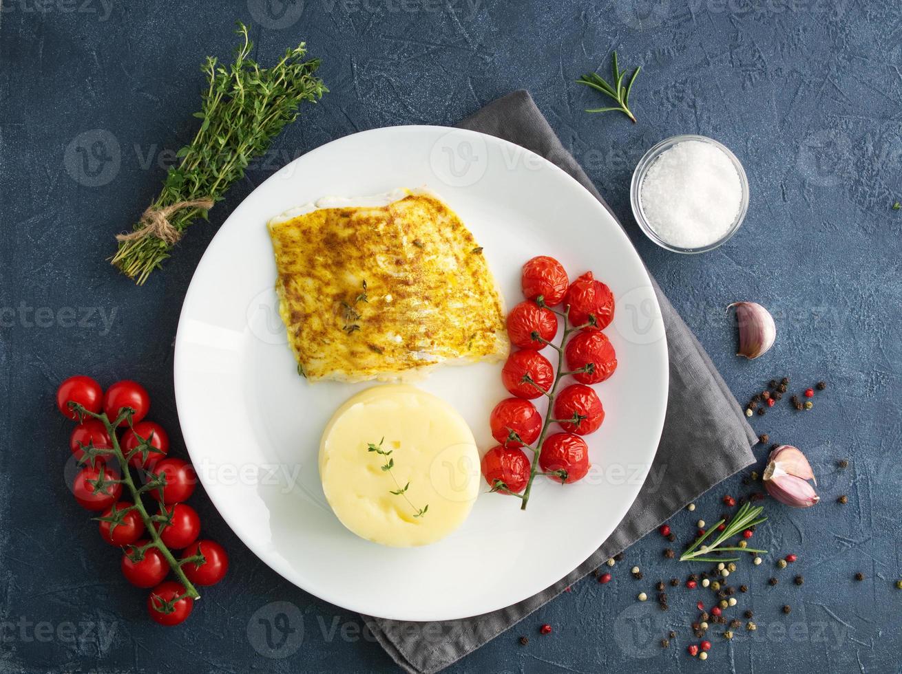 Im Ofen gebackener Kabeljau mit Kartoffelpüree, Tomaten, gesunde Ernährung. dunkelgrauer Hintergrund foto