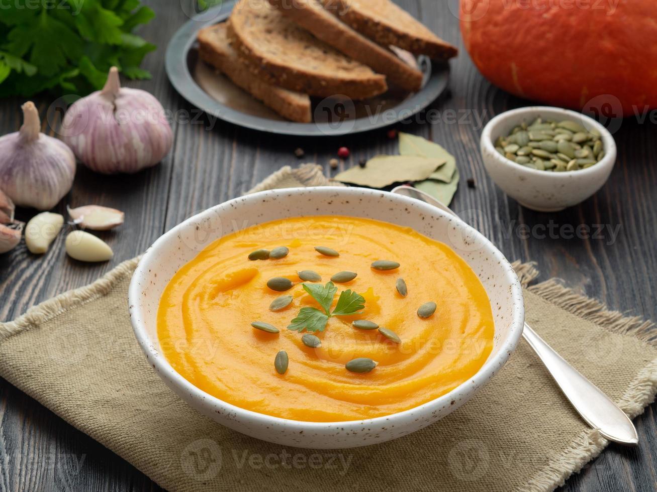 Kürbissuppe püriert in einem weißen Teller, Kürbiskerne, Brot, Knoblauch auf dunklem Holzhintergrund foto