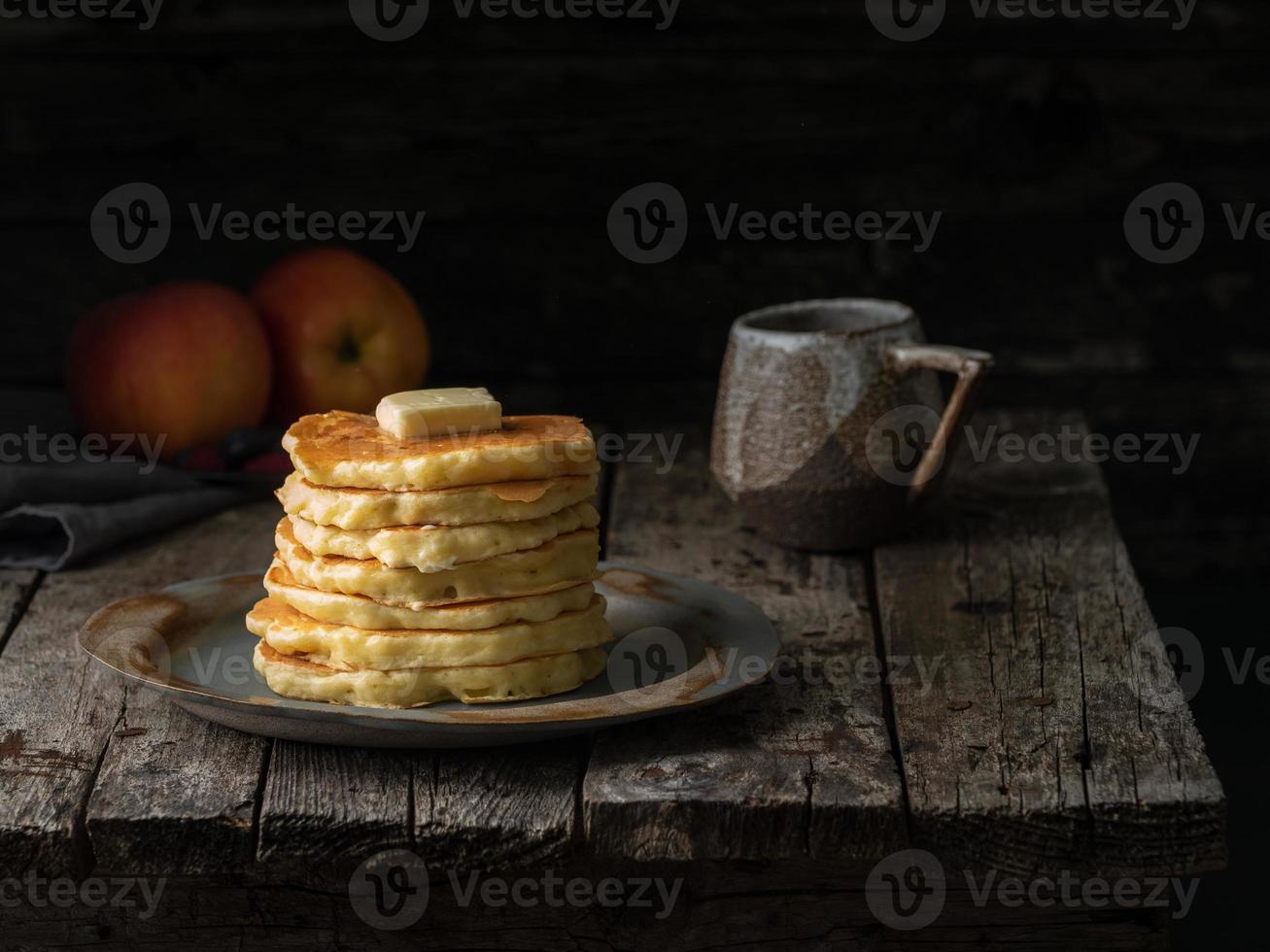 Pfannkuchen mit Butter und Tasse Tee. dunkler, launischer alter rustikaler Holzhintergrund. foto