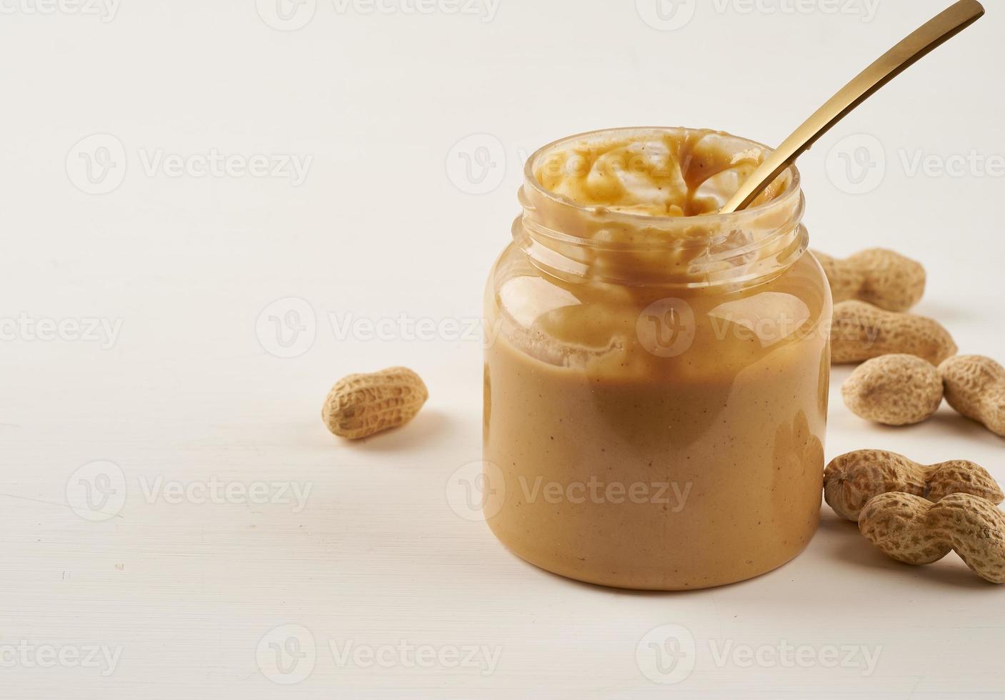 Glas Erdnussbutter und Erdnüsse in der Schale auf weißem Tisch, Seitenansicht, foto