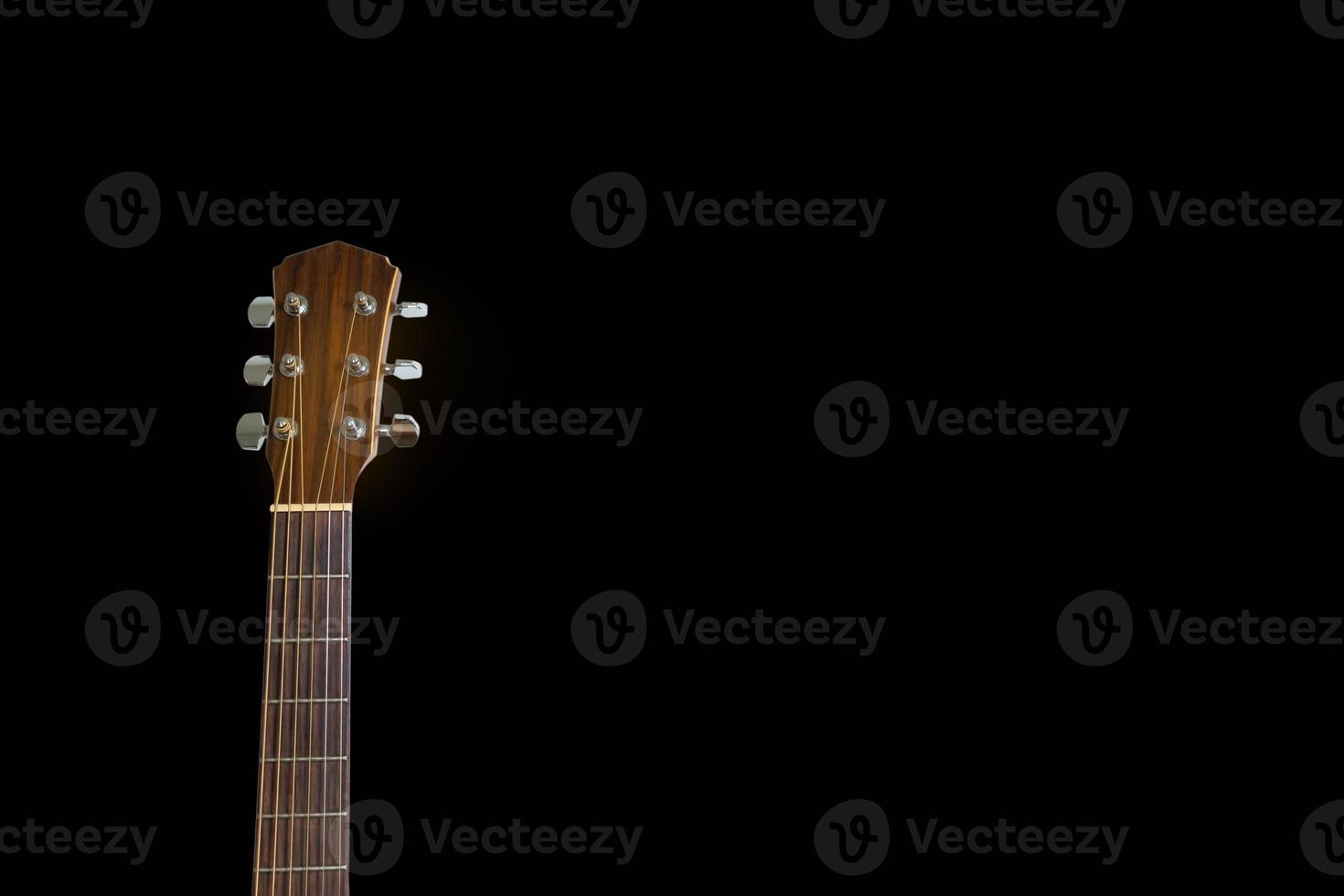 Der isolierte Kopf einer Akustikgitarre lehnte sich gegen den dunklen schwarzen Hintergrund. Platz kopieren. foto