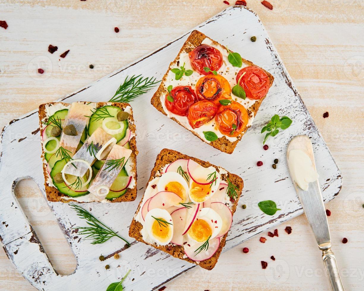 Smorrebrod - traditionelle dänische Sandwiches. Schwarzes Roggenbrot mit Hering, Ei, Tomaten, Rettich auf weißem Holztisch, Draufsicht foto