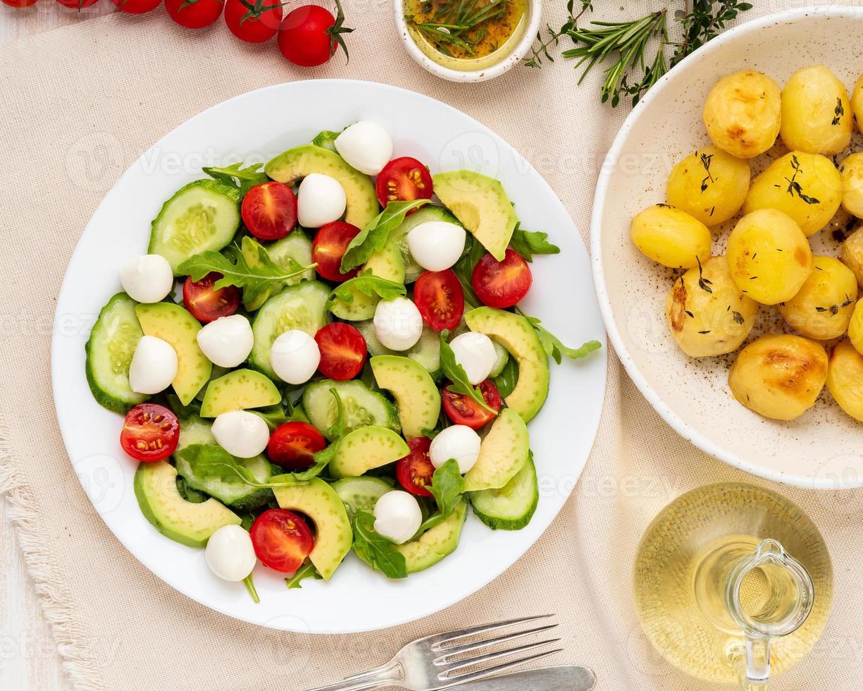 Frischer Salat mit Tomaten, Gurken, Rucola, Mozzarella und Avocado. Öl mit Gewürzen, Bratkartoffeln, Draufsicht, vertikal foto