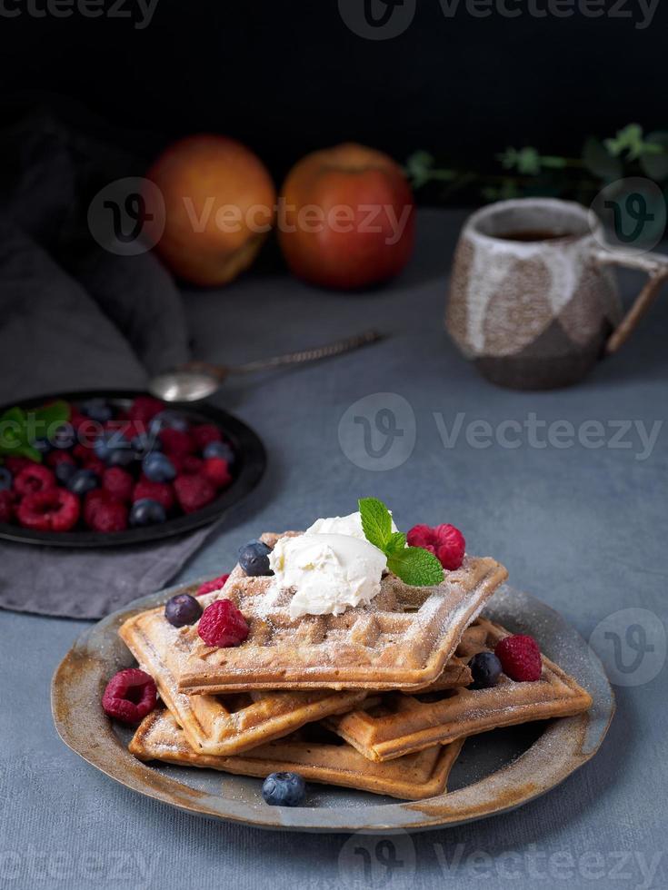 Belgische Waffeln mit Himbeeren, Schokoladensirup. Frühstück mit Tee auf dunklem Hintergrund, Seitenansicht, vertikal foto