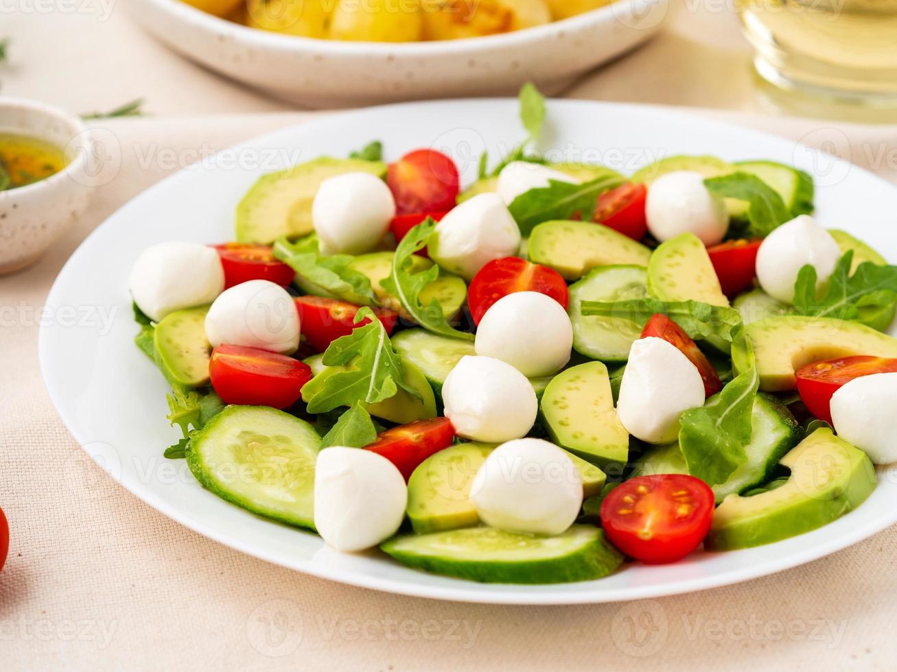 Frischer Salat mit Tomaten, Gurken, Rucola, Mozzarella und Avocado. Öl mit Gewürzen Rosmarin Thymian, Seitenansicht hautnah foto