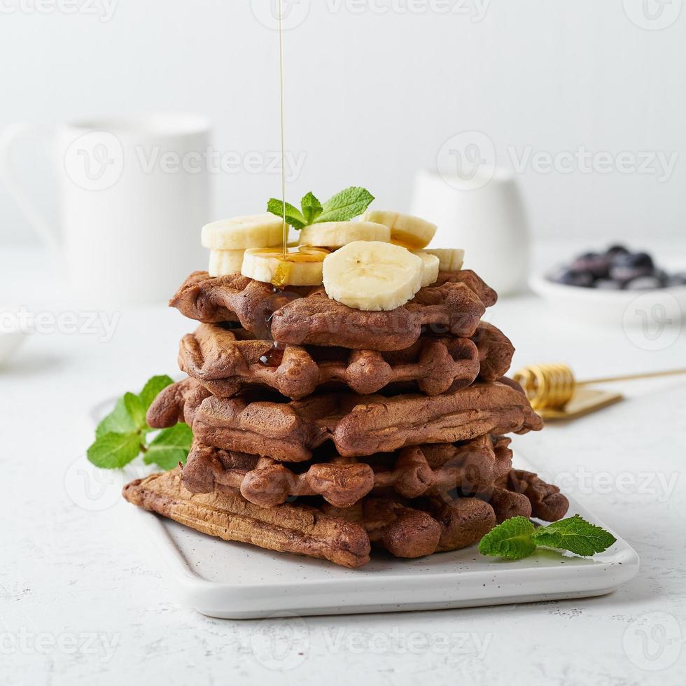 Schokoladen-Bananen-Waffeln mit Ahornsirup auf weißem Tisch, Seitenansicht. süßer Brunch, Ahornsirupfluss foto