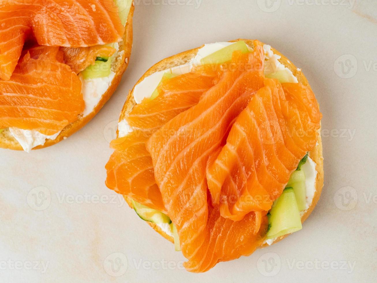 Zwei offene Sandwiches mit Lachs, Frischkäse, Gurkenscheiben auf weißem Marmortisch foto