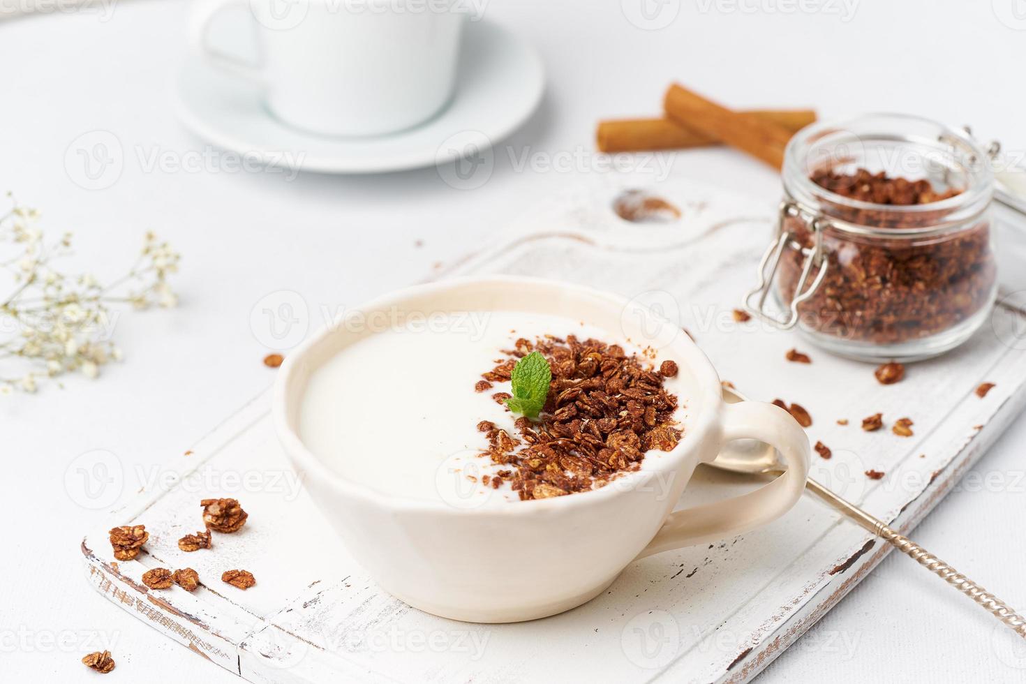 joghurt mit schokoladenmüsli in der tasse, frühstück mit tee auf weißem holzhintergrund, seitenansicht. foto