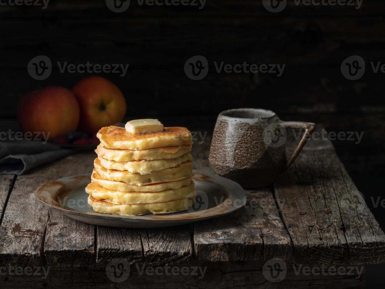 Pfannkuchen mit Butter und Tasse Tee. dunkler, launischer alter rustikaler Holzhintergrund. foto