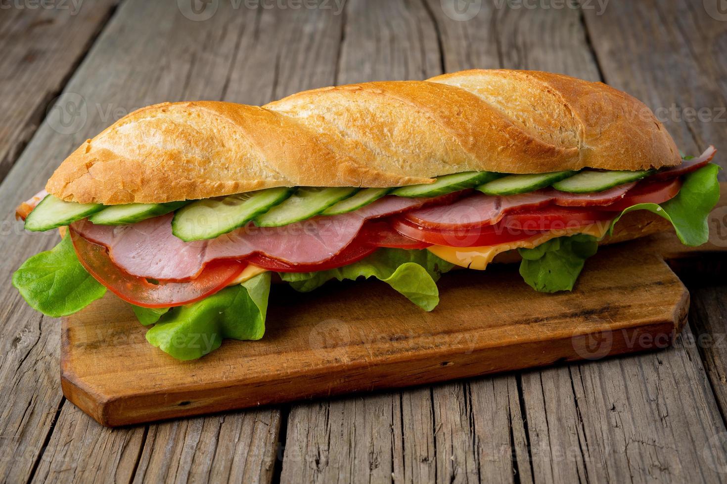 Sandwich mit Schinken, Käse, Tomaten, Gurken, Salat auf dunklem Holzhintergrund foto