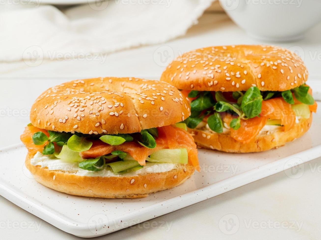 Zwei Sandwiches mit Lachs, Frischkäse, Gurkenscheiben auf weißem Marmortisch foto