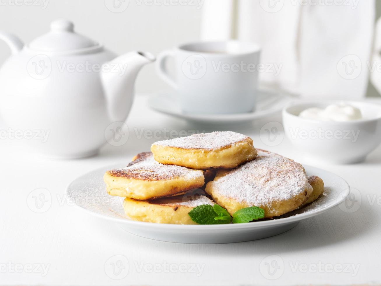 Käsekuchen, Quarkkrapfen. Quarkpfannkuchen mit Puderzucker. süße gebratene Käsepfannkuchen auf weißer Platte auf weißem Hintergrund. Teeparty zu Hause foto