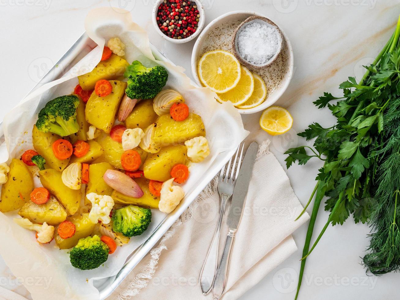 gebratenes Gemüse auf Tablett mit Pergament auf Marmortisch. Kartoffeln, Karotten, foto