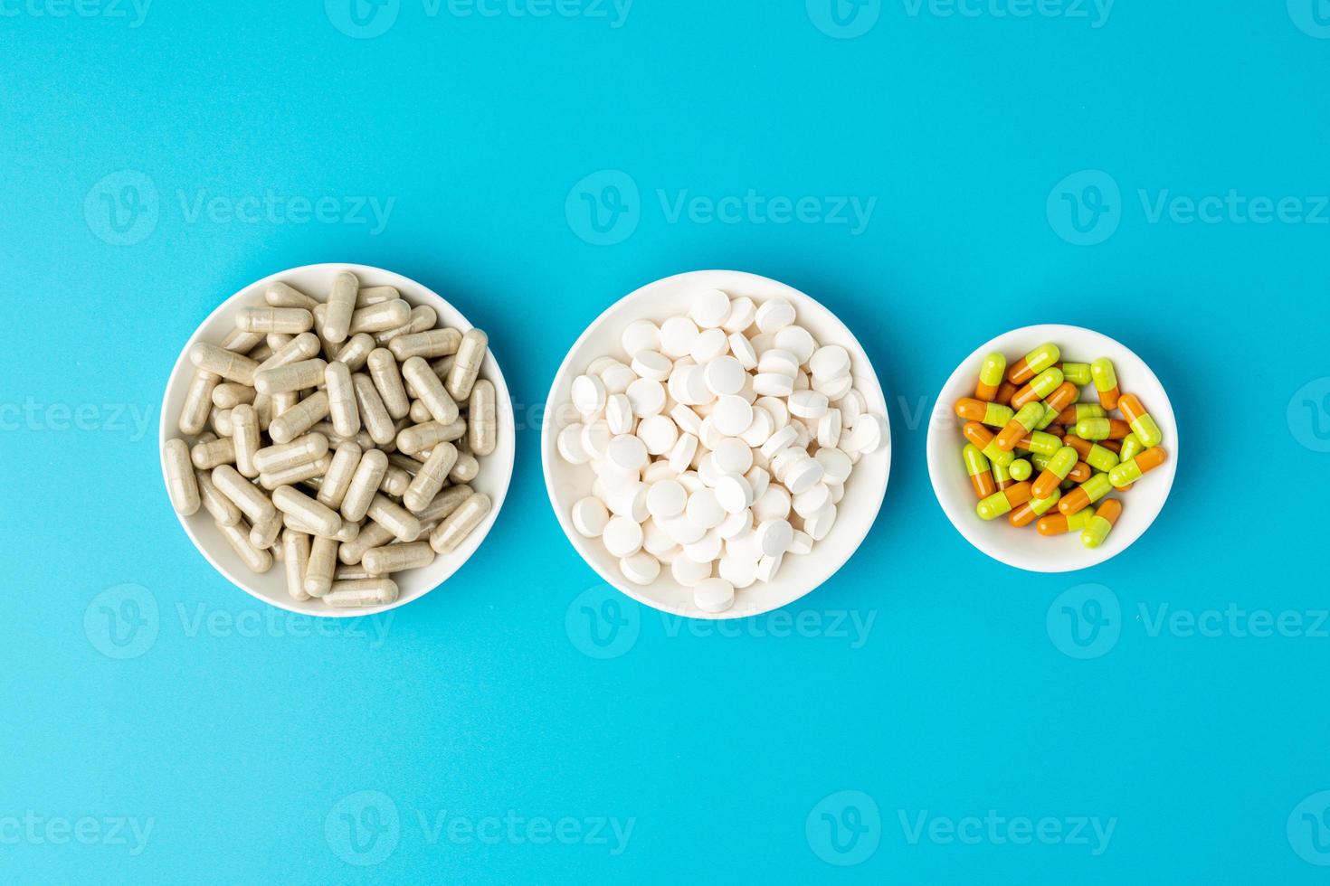 Türkisfarbener Hintergrund einer großen Gruppe verschiedener Kapseln, Pillen und Tabletten in weißen Schalen hintereinander foto