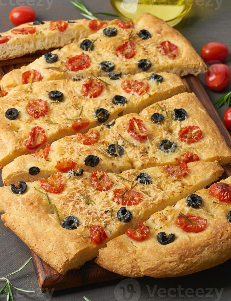 Focaccia, Pizza, italienisches Fladenbrot mit Tomaten, Oliven und Rosmarin auf dunkelbraunem Tisch foto