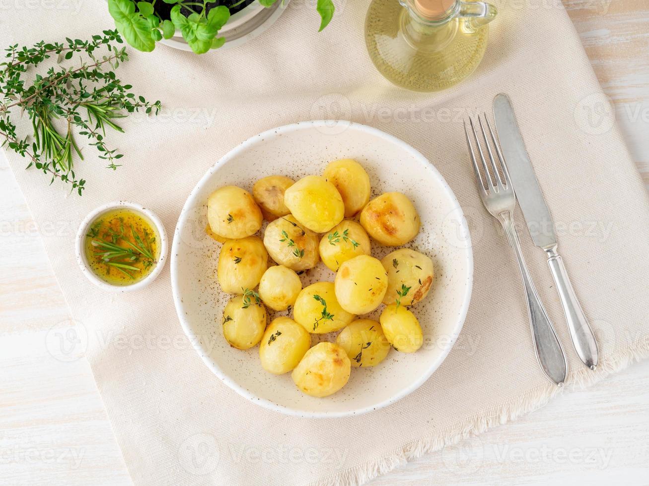 im Ofen gebacken mit Gewürzen runden ganzen Kartoffelknollen in Platte auf weißem Textilhintergrund foto