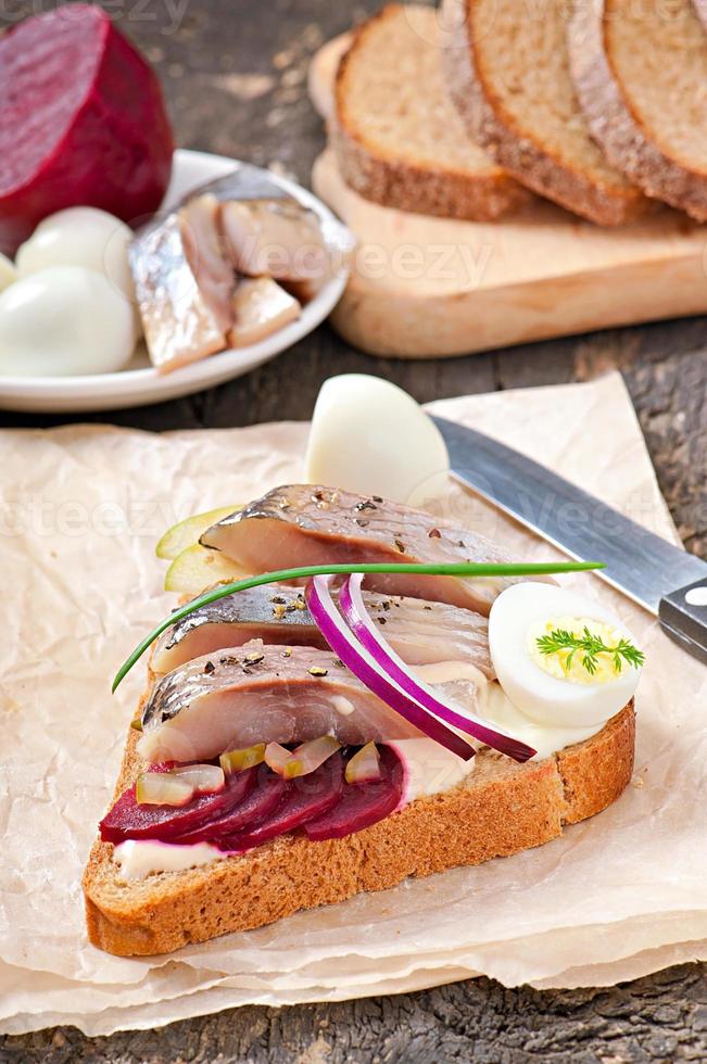 Sandwich aus Roggenbrot mit Hering, Rüben, Zwiebeln und Ei foto