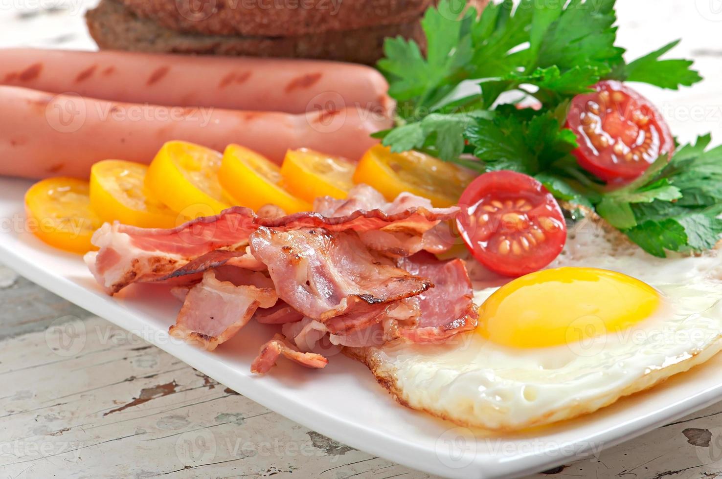 Englisches Frühstück - Spiegeleier, Speck, Würstchen und geröstetes Roggenbrot foto