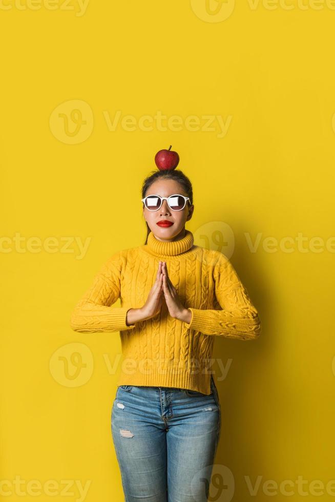 fröhliche junge Frau auf gelbem Hintergrund im Studio. ein Mädchen mit einem Apfel, der beim Yoga auf dem Kopf ruht. das Konzept der Bewegung für eine gute Gesundheit. Gesundheitsliebhaber foto