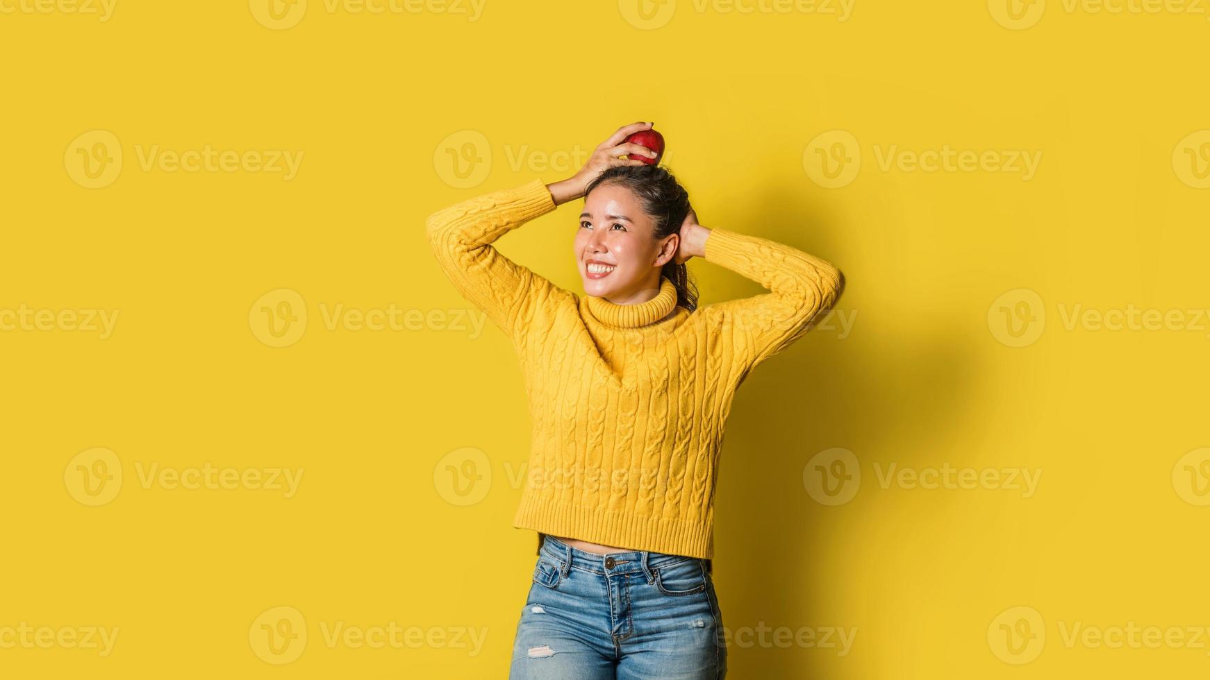 fröhliche junge Frau auf gelbem Hintergrund im Studio. ein Mädchen mit einem Apfel, der beim Yoga auf dem Kopf ruht. das Konzept der Bewegung für eine gute Gesundheit. Gesundheitsliebhaber foto