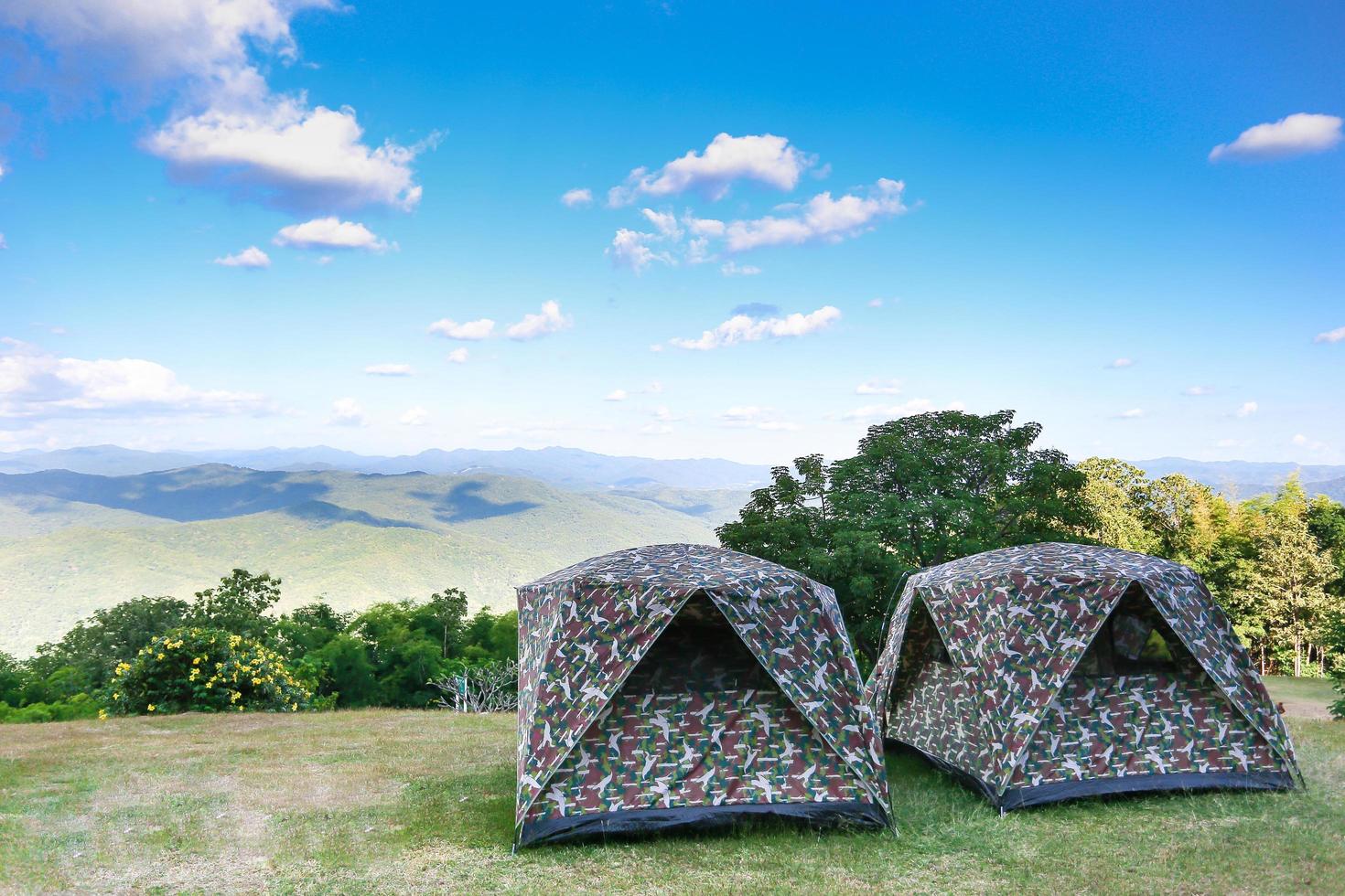 Zelt auf dem Hügel unter den Bergen unter klarem Himmel im schönen Sommerlandschaftslager. Das Tarnzelt steht bei Sonnenaufgang als Naturtapete auf grünen Feldern und Bergen foto