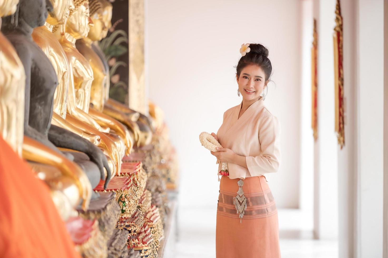 schöne thailändische frauen in traditioneller thailändischer kleidung verwenden frische blumengirlanden, um dem buddha-bild zu huldigen, um sich auf dem thailändischen songkran-fest etwas zu wünschen foto