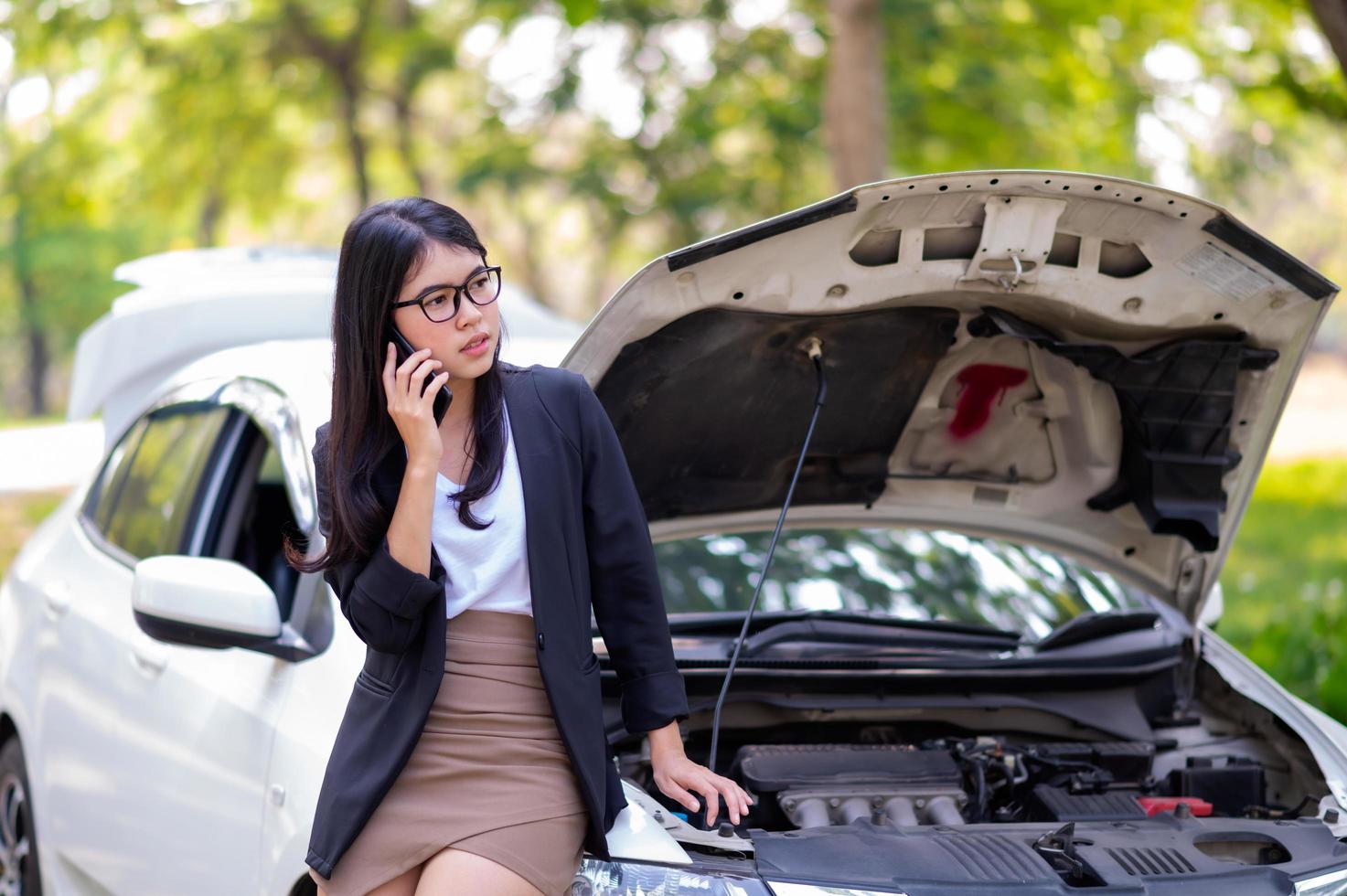 eine junge asiatin ruft ihren servicetechniker an, um ein kaputtes auto am straßenrand zu reparieren foto