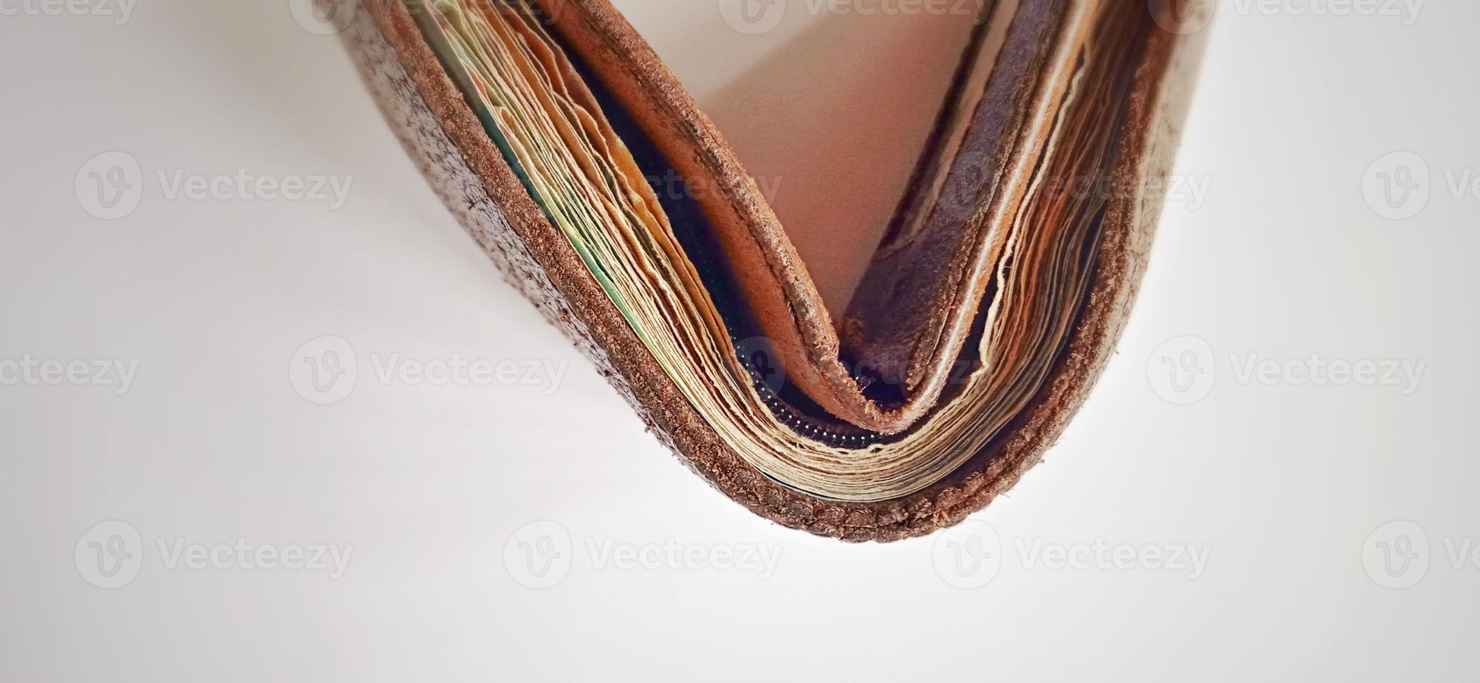 Eine alte braun-orangefarbene synthetische Brieftasche mit etwas Geld darin auf dem schwach grau-gelben Hintergrund. foto