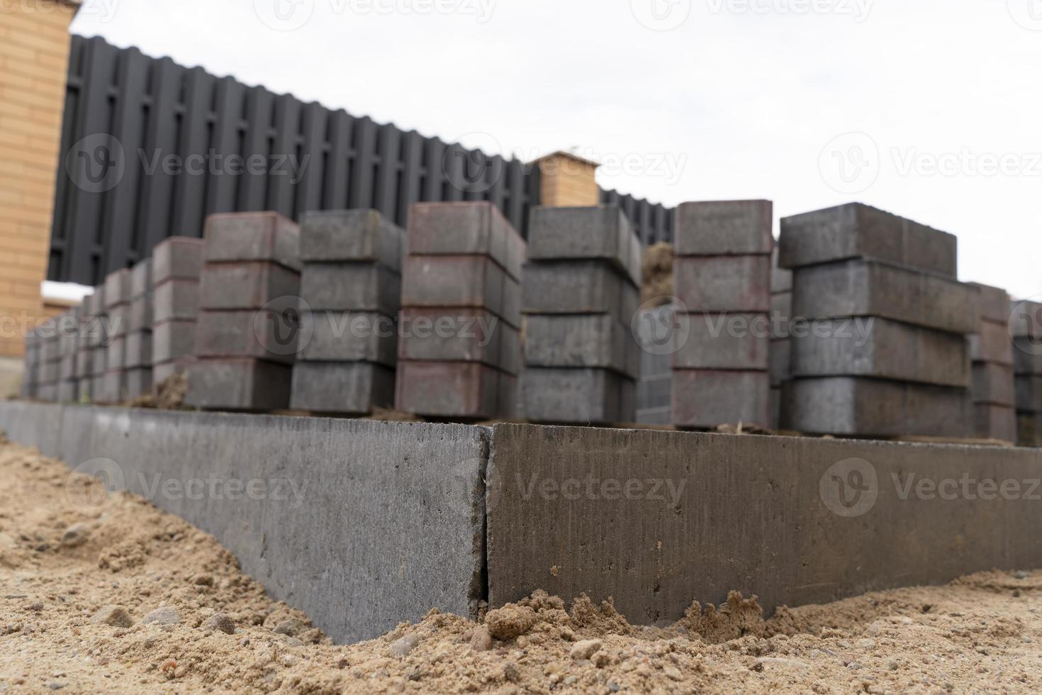 Verlegung von grauen Betonplatten in der Hofeinfahrt des Hauses. Professionelle Maurer verlegen neue Fliesen oder Platten für die Einfahrt, den Bürgersteig oder die Terrasse auf einem flachen sandigen Untergrund. foto