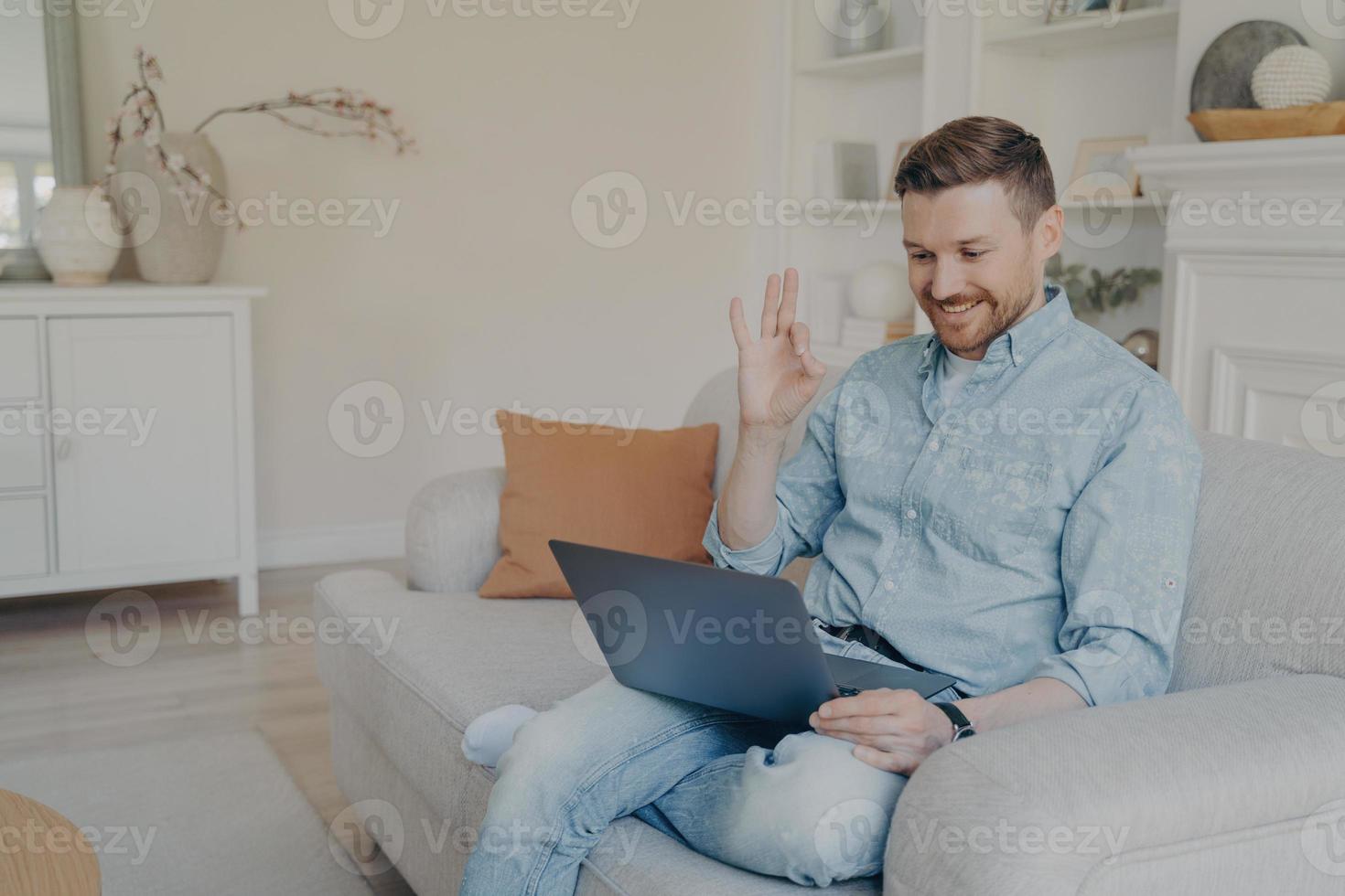 junger männlicher büroangestellter, der während des online-meetings zu hause eine okay-geste zeigt foto