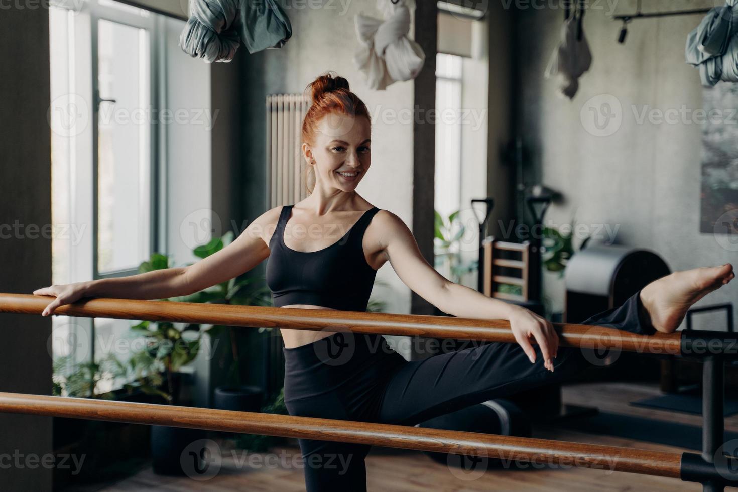 glückliche junge frau, die sich während des barre-trainings im fitnessstudio gut ausdehnt foto